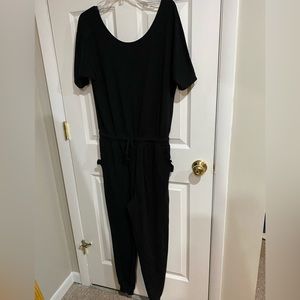 Wavvy black jumpsuit with tie waist, 2 ruffled slit side pockets. Ribbed cuff.